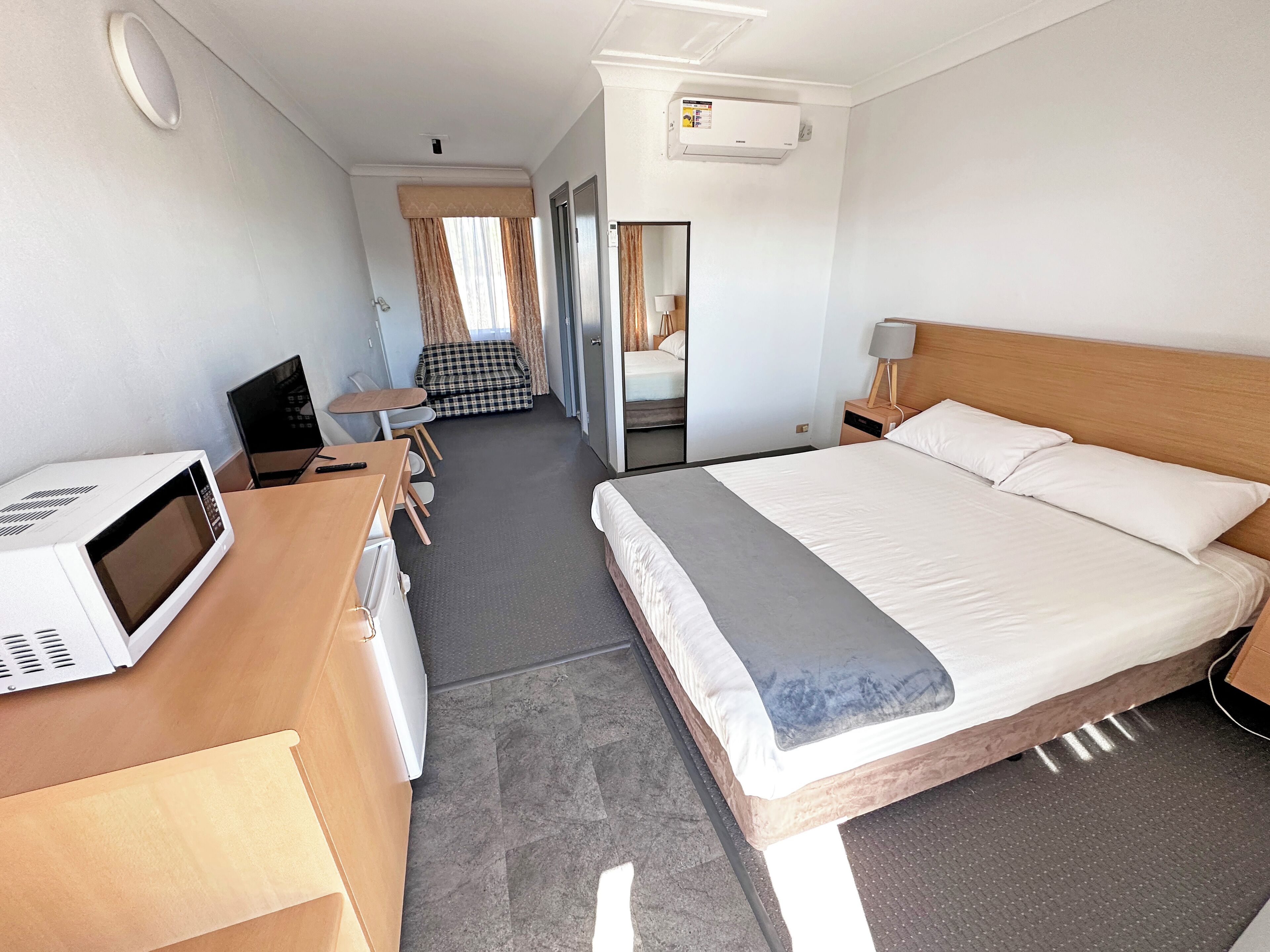 A hotel room with a bed, a desk with a microwave, a chair, a table, and a sofa.