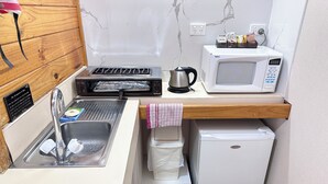 A compact kitchenette with a sink, toaster, kettle, microwave, and a small refrigerator. - Spa Village Motel (Moree)