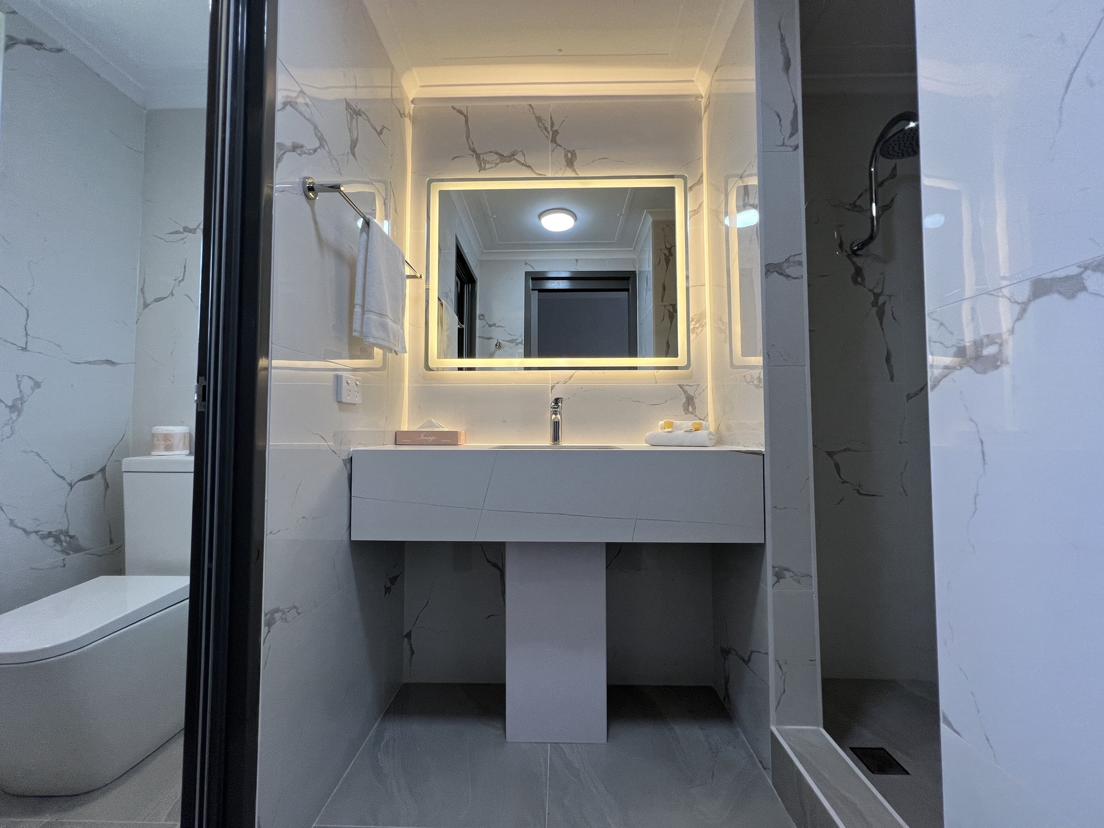 A modern bathroom with a marble vanity, a large mirror, and a shower area.