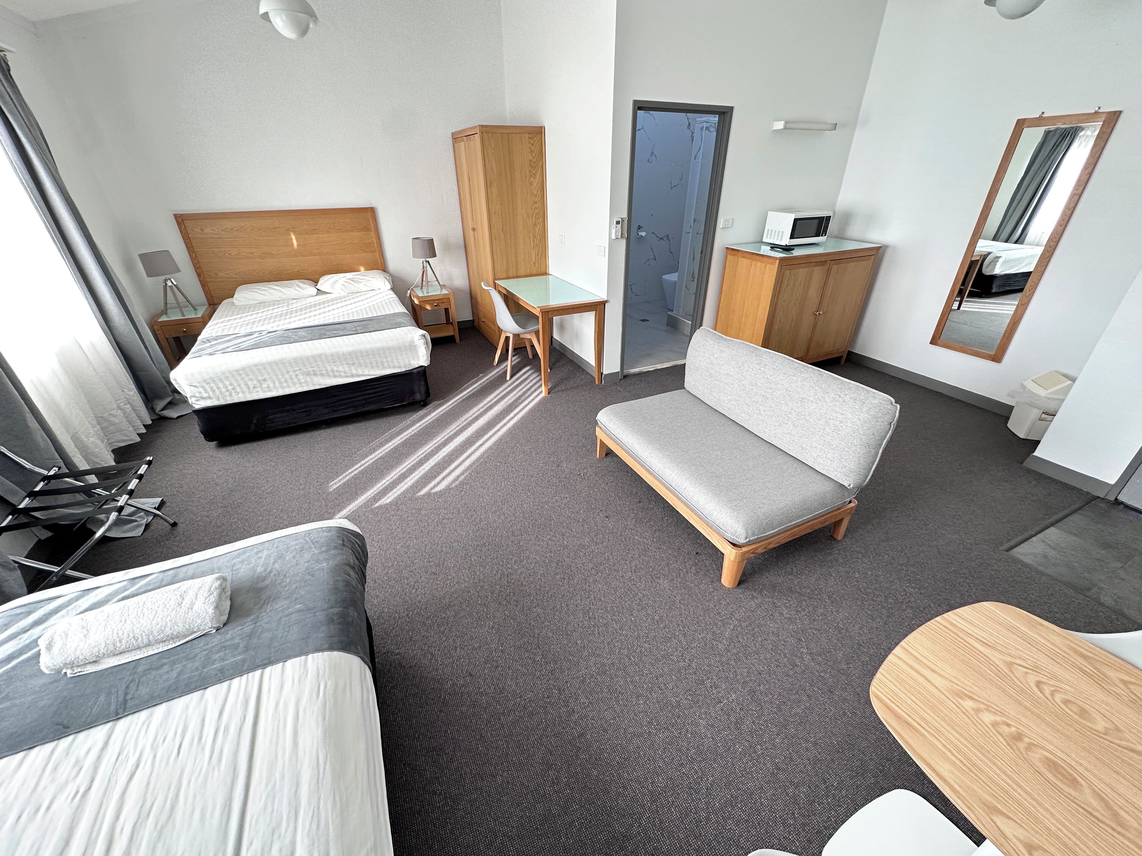 A hotel room with two beds, a sofa, a desk, a mirror, and a wardrobe.