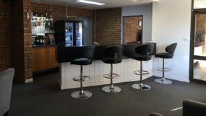 A bar area with a brick wall, a refrigerator stocked with beverages, and three black bar stools. - Spa Village Motel (Moree)