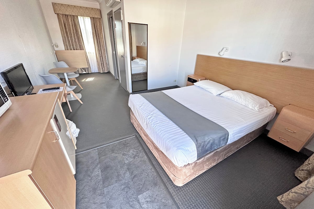 A hotel room with a bed, bedside tables, a desk with a computer, a chair, a mirror, and a wardrobe.