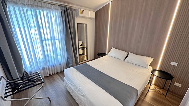 A modern hotel room with a large bed, a bedside table, a chair, and a window with curtains. - Spa Village Motel (Moree)
