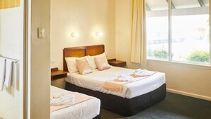 A hotel room with two single beds, a nightstand, a window with curtains, and a view of the outside. - Town & Country Motel (Strathfield)