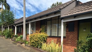 A row of single-story houses with brick exteriors and tiled roofs, featuring large windows and a well-maintained front yard with various plants. - Town & Country Motel (Strathfield)