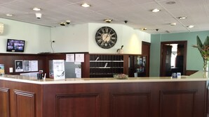 A reception area with a wooden counter, a wall clock, and a television displaying news. - Town & Country Motel (Strathfield)