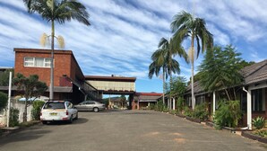 A street view with a building that has a red brick facade and a balcony. There are palm trees and a covered walkway. - Town & Country Motel (Strathfield)