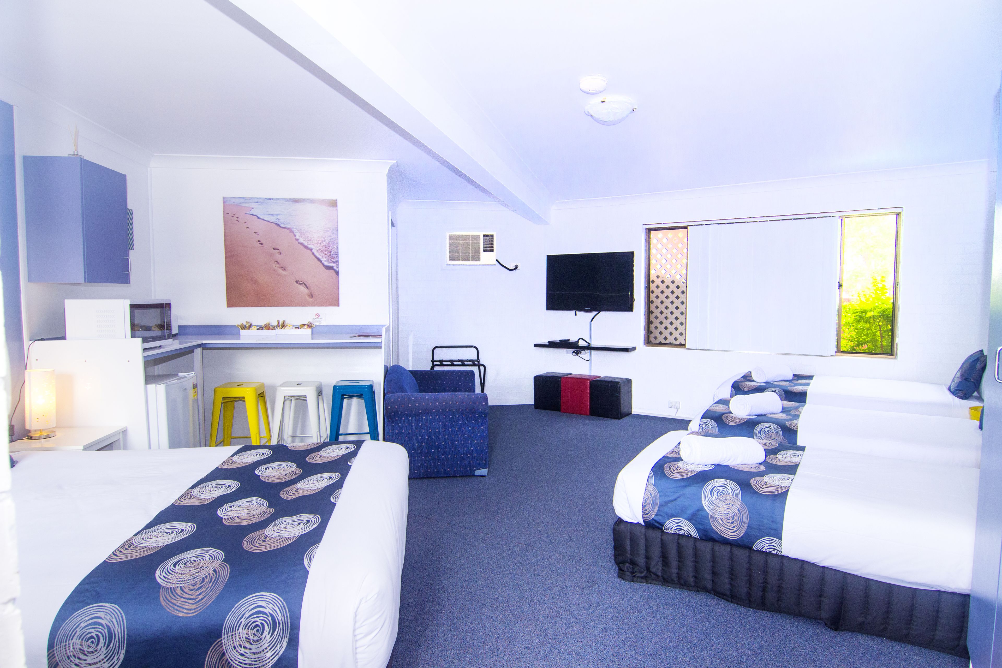 A hotel room with two beds, a desk, a chair, a TV, and a painting on the wall.