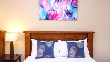 A neatly made bed with two pillows, a wooden headboard, and a wall-mounted abstract painting.