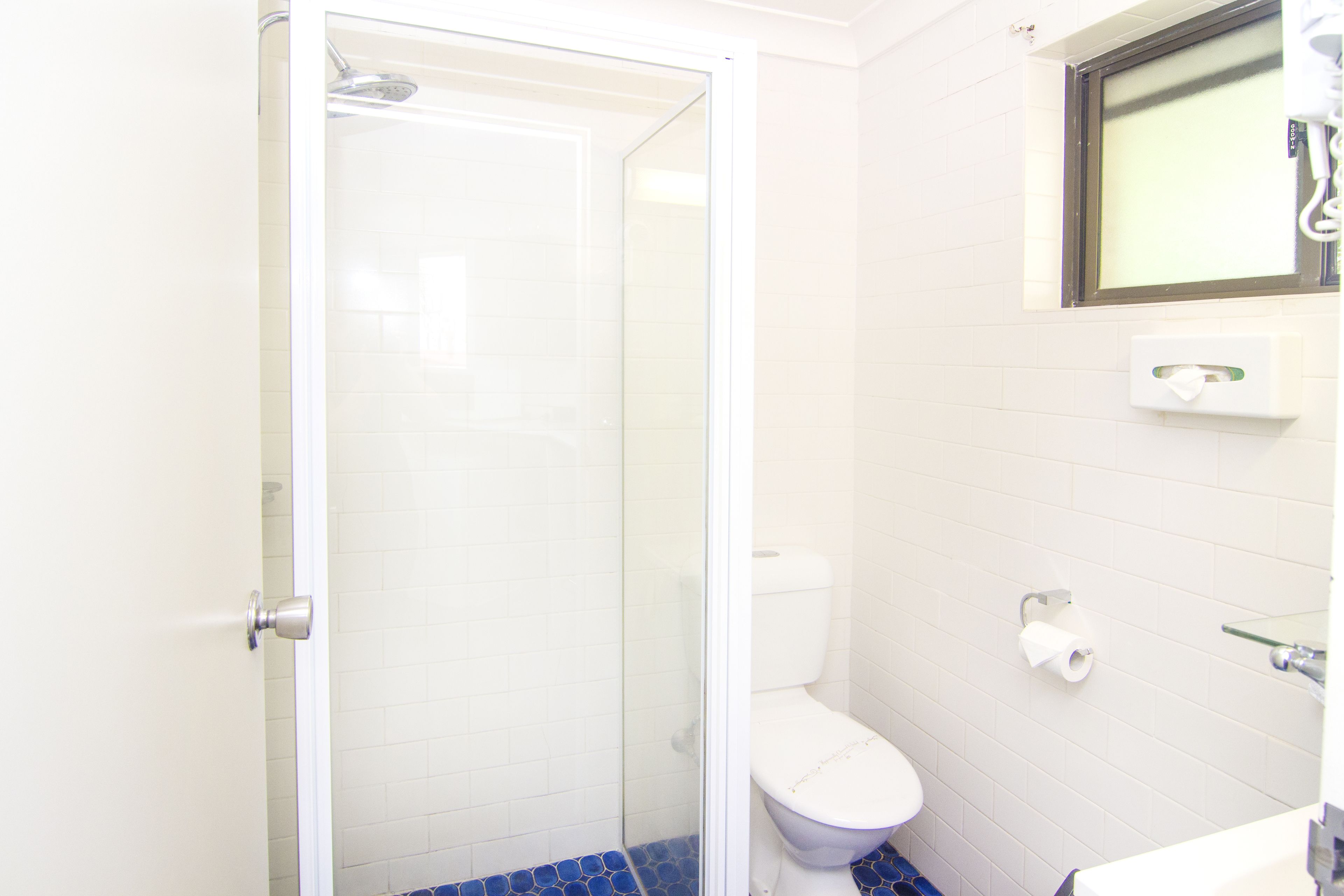 A bathroom with a glass-enclosed shower, a white toilet, and a small window above the sink.