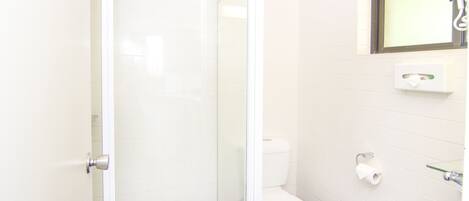 Un baño con cabina de ducha de vidrio, inodoro blanco y una pequeña ventana sobre el lavamanos.