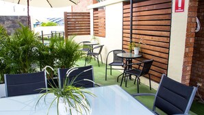 An outdoor patio with a glass table surrounded by chairs, potted plants, and a brick wall. - Crescent Motel (Taree)