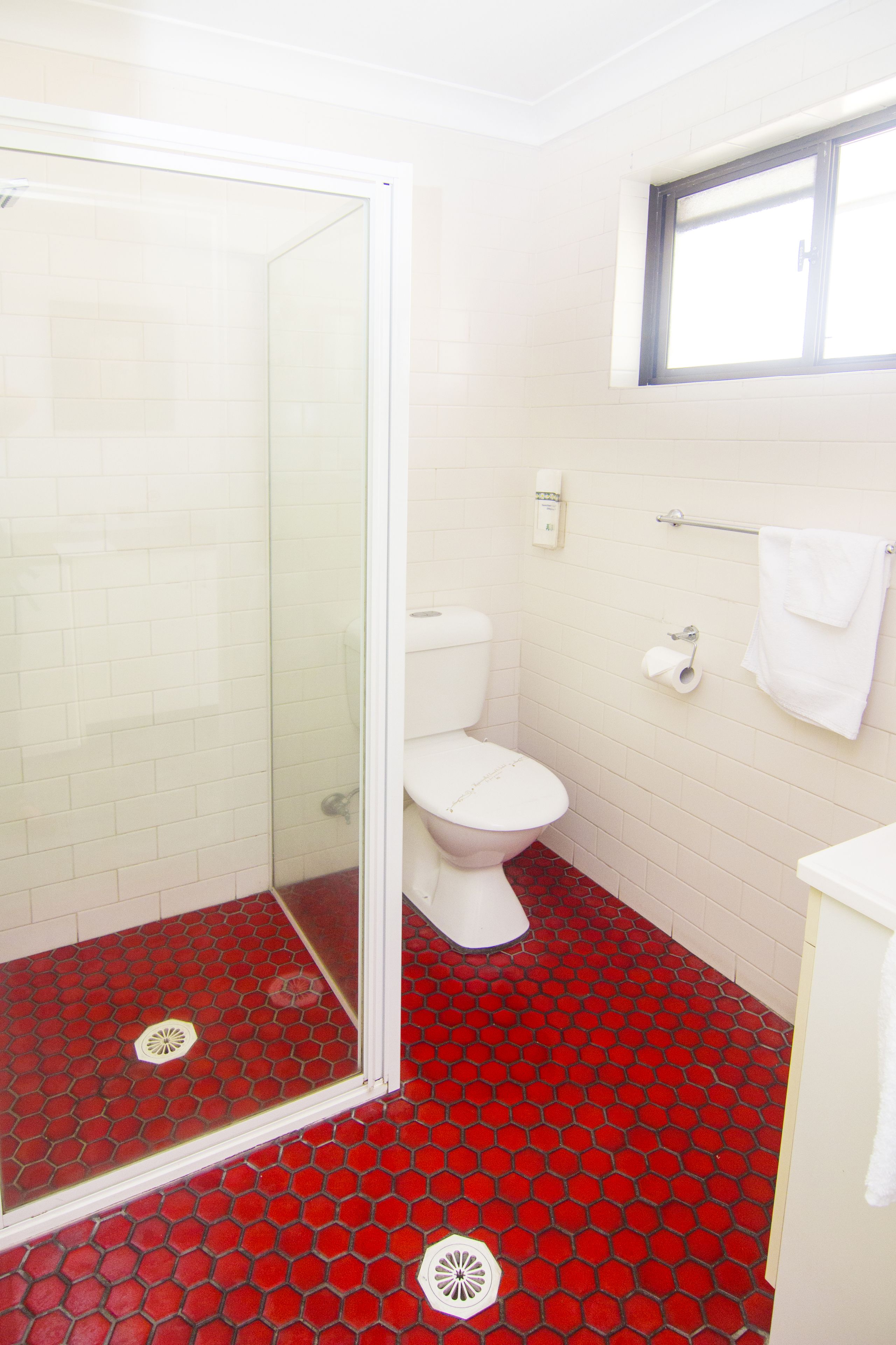 A bathroom with a glass shower enclosure, a white toilet, and a red-tiled floor.