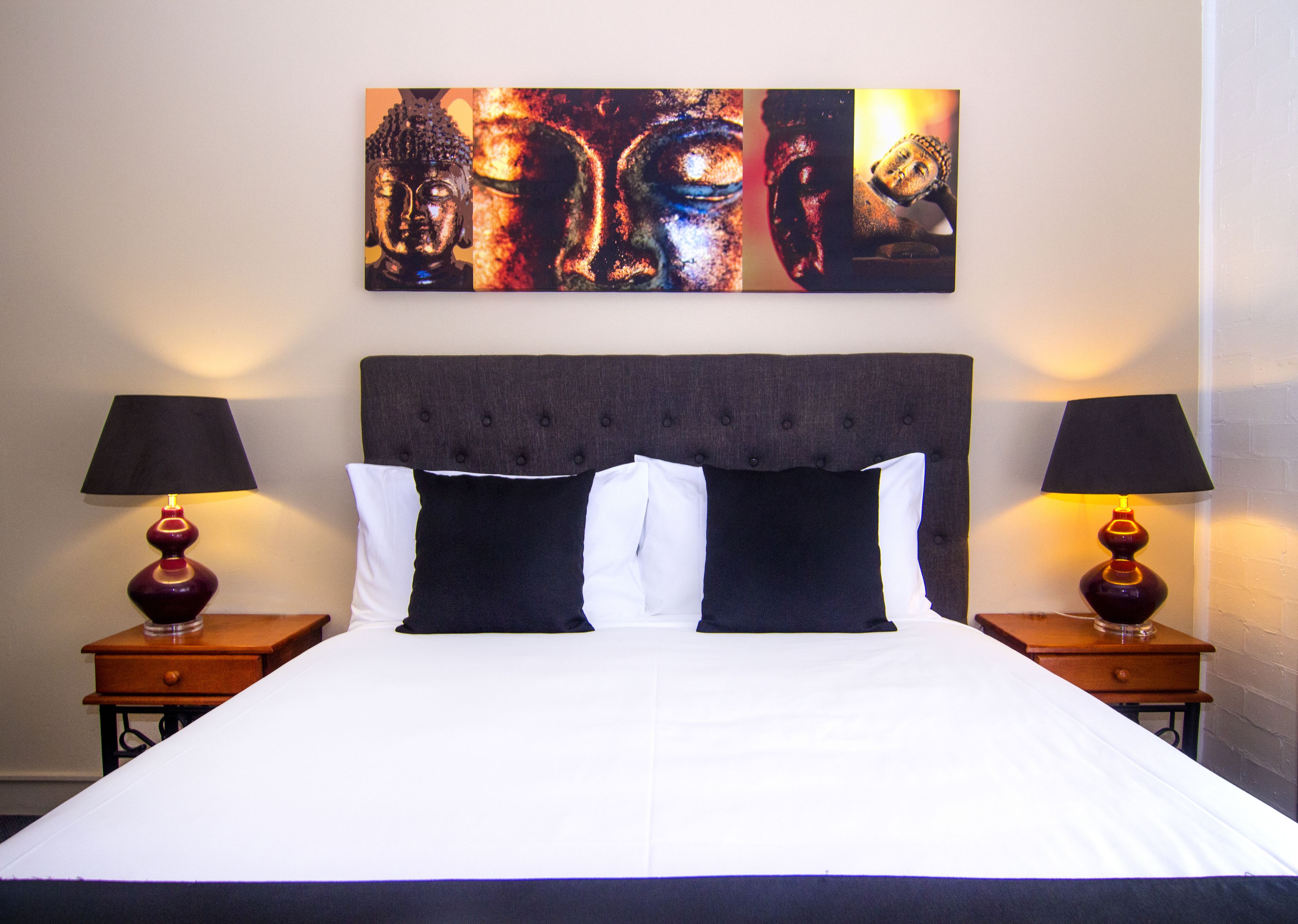Una cama con cabecera oscura, dos mesitas de noche con lámparas, y un cuadro abstracto grande sobre la cama.