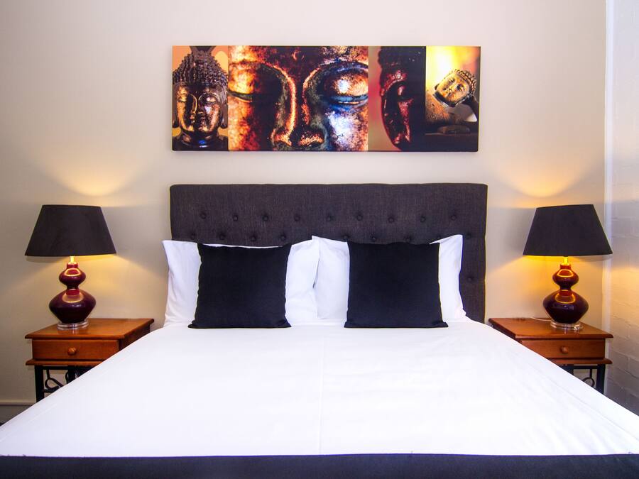 Una cama con cabecera oscura, dos mesitas de noche con lámparas, y un cuadro abstracto grande sobre la cama.