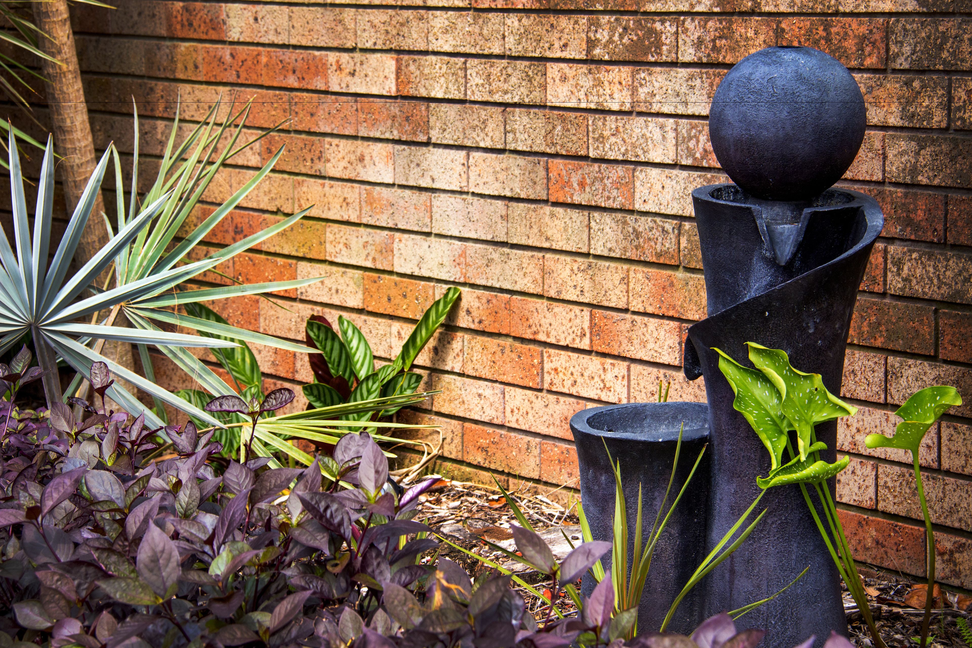 A garden with a brick wall, various plants, and a black sculpture.