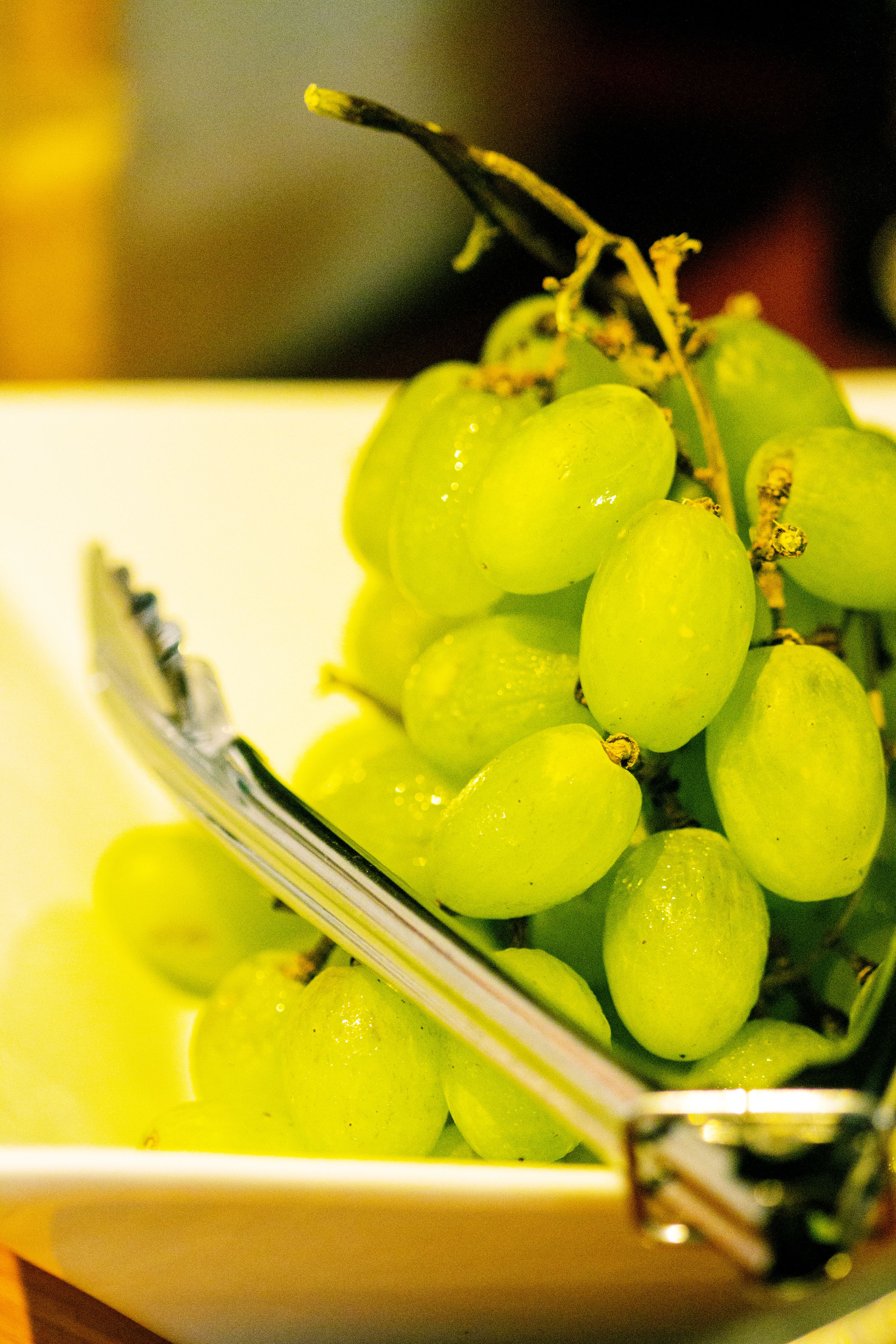 Un tazón de uvas verdes con un par de pinzas encima.