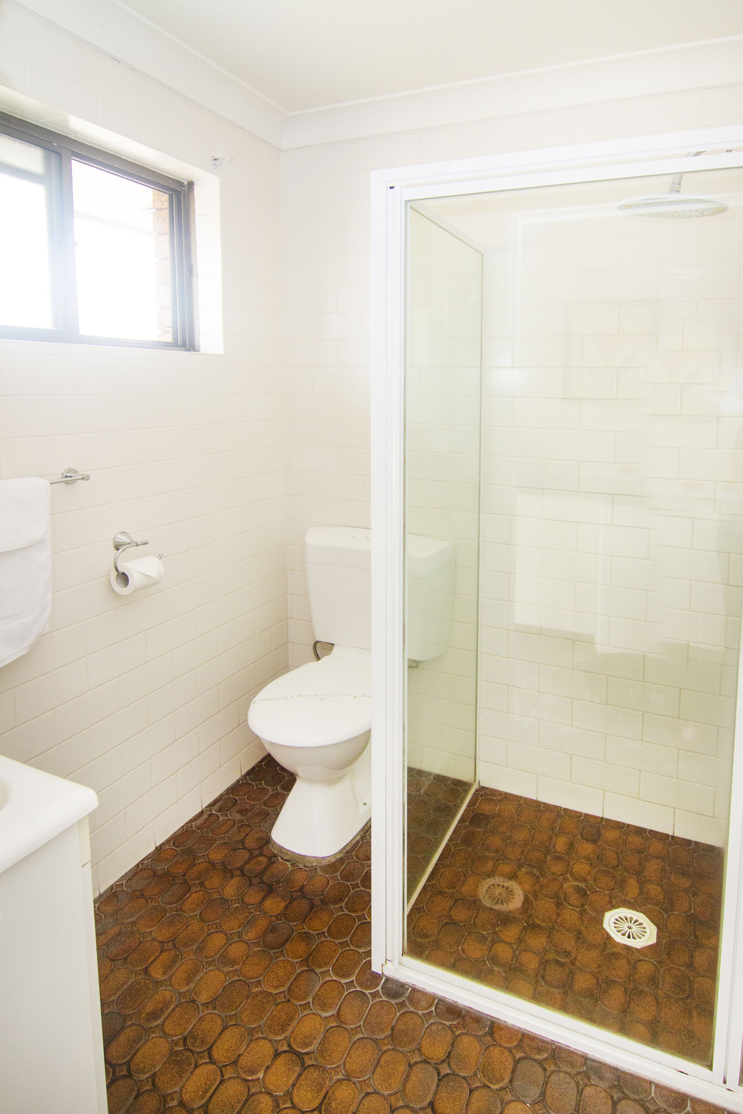 Een badkamer met een wit toilet, een douche met glazen wanden en een vloer met een patroon.
