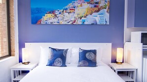 A hotel room with a large bed, two bedside tables, and a wall-mounted painting of a coastal town. - Crescent Motel (Taree)