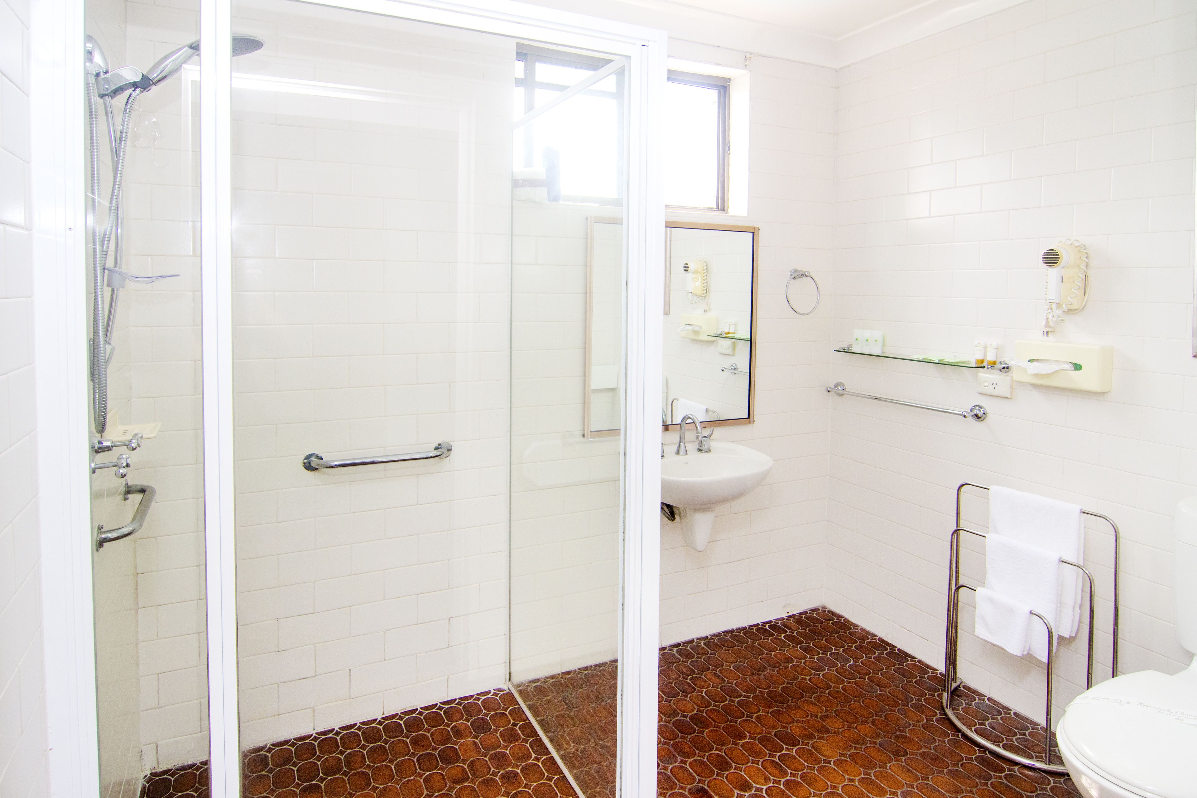 A bathroom with a glass shower enclosure, a white sink, and a tiled floor.