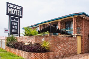 Un motel de ladrillo con un cartel que anuncia servicios como aire acondicionado, barbacoa, piscina y Wi-Fi.