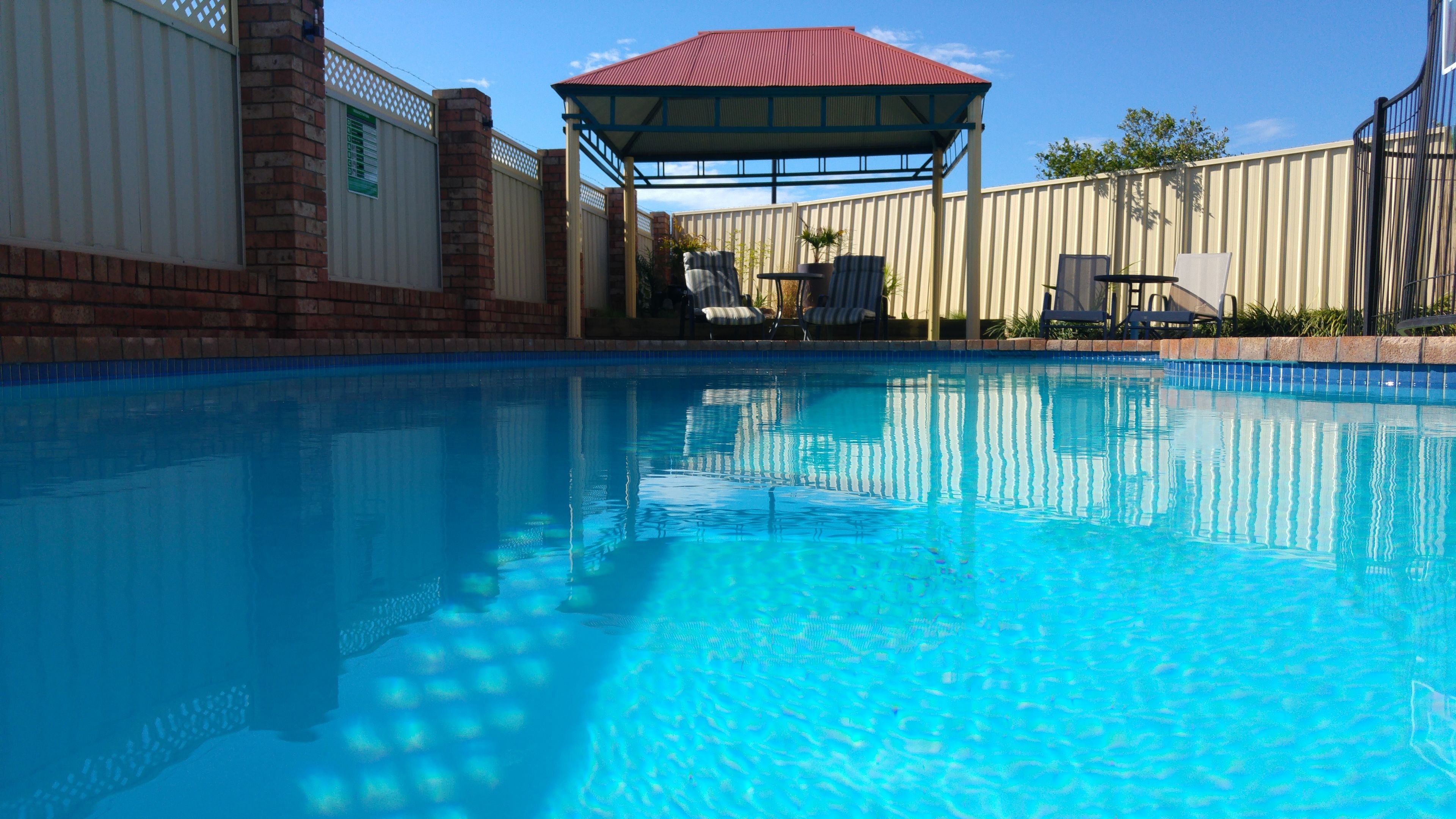 A swimming pool with a covered seating area and a fence.