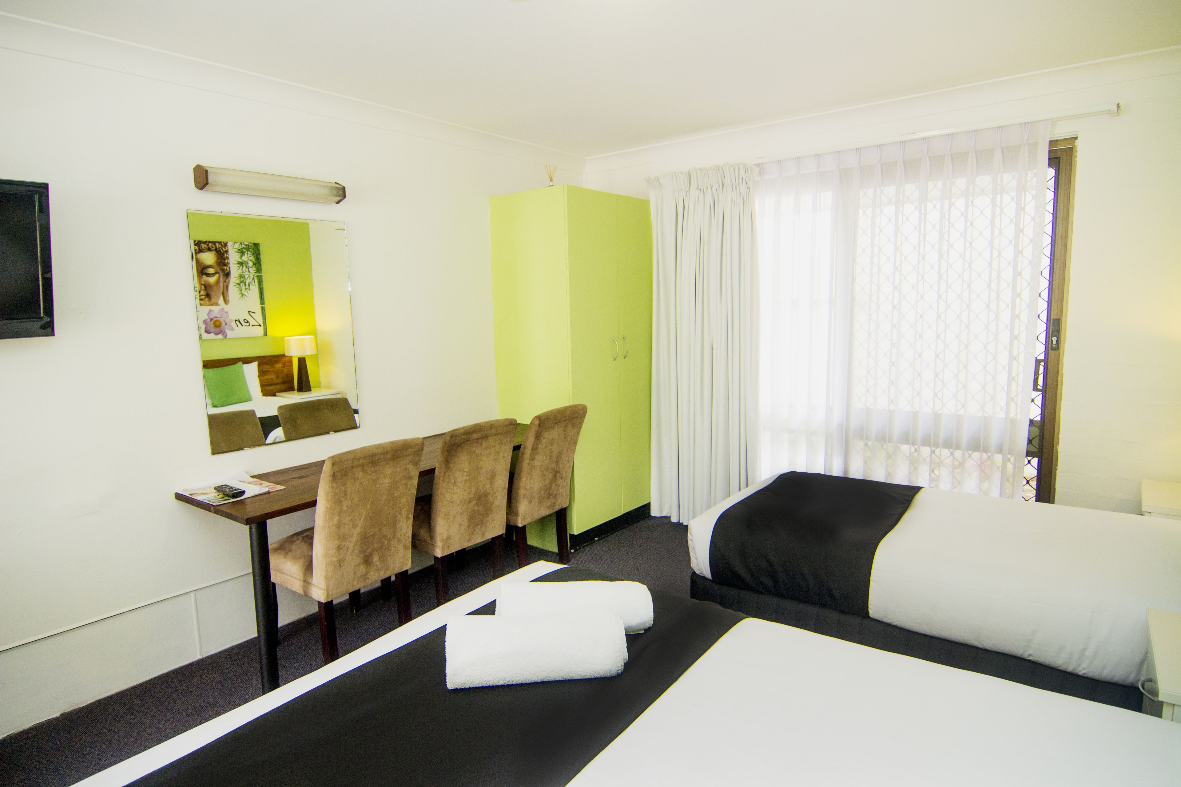 A hotel room with a bed, a desk with chairs, a mirror, and a window with curtains.