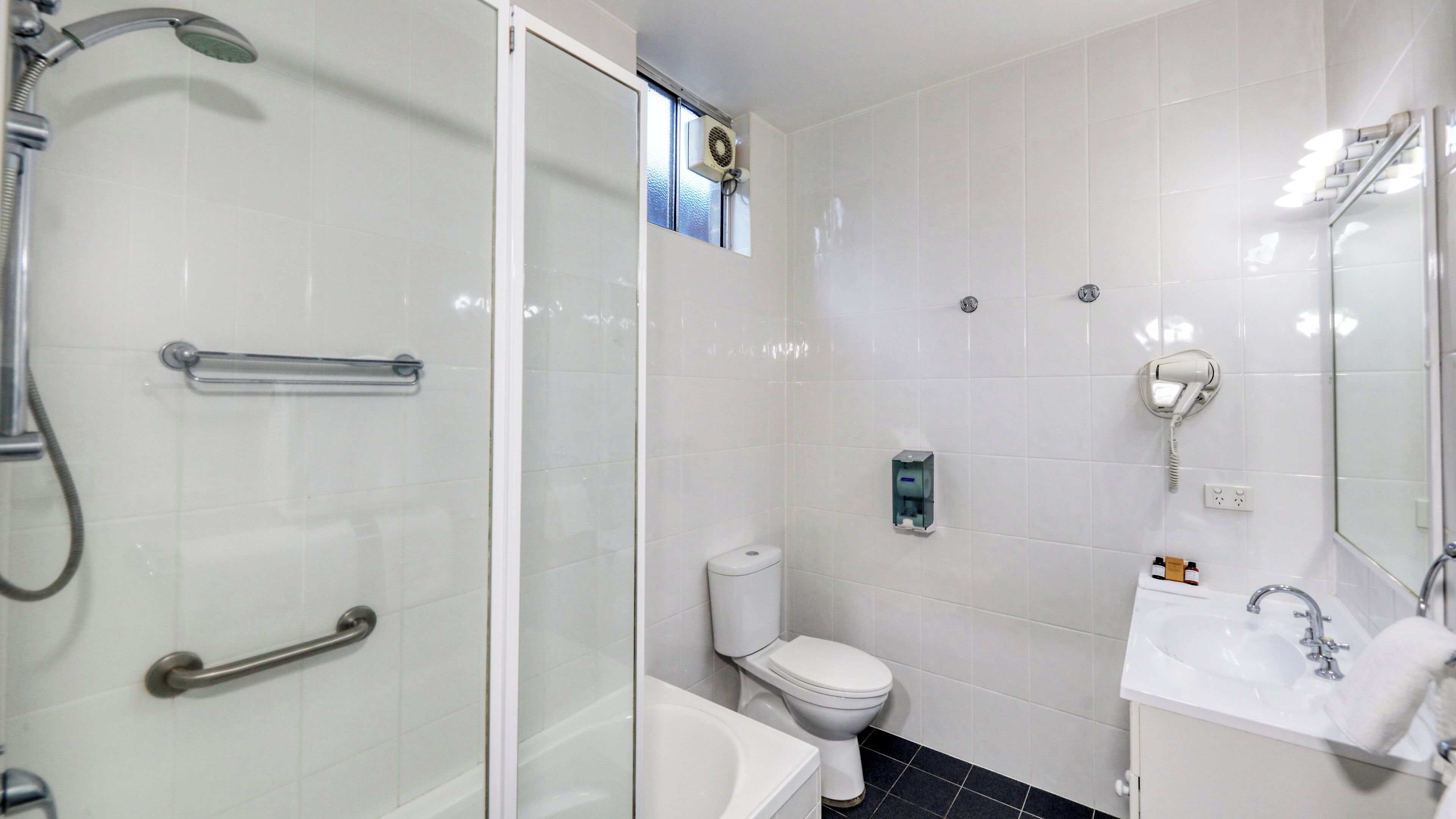 Une salle de bain moderne avec une douche à parois de verre, des toilettes, un lavabo et un sèche-cheveux fixé au mur.