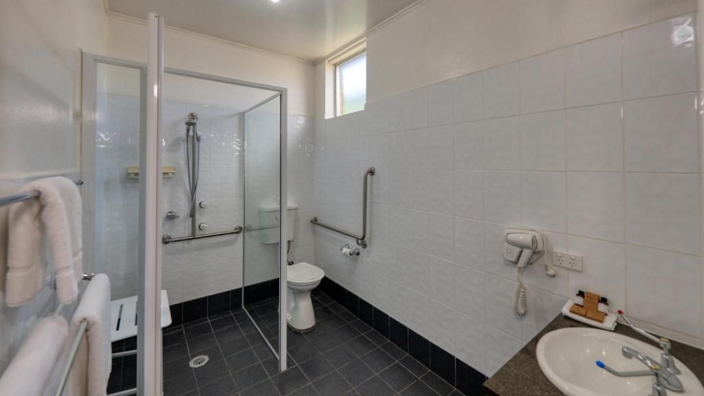 Et badeværelse med brusekabine i glas, toilet, håndvask og hårtørrer.