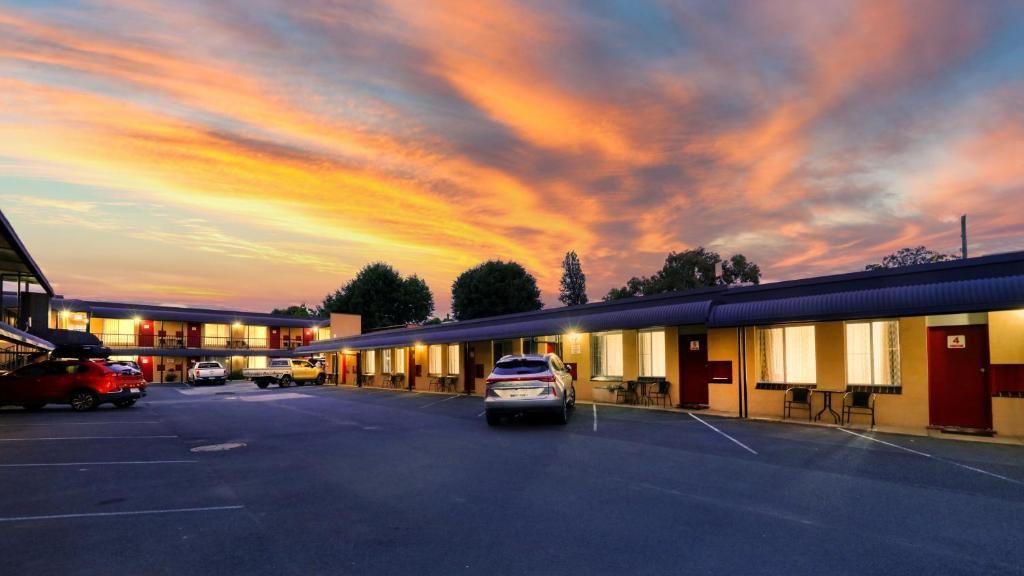 Ein Motel mit mehreren Zimmern, einem Parkplatz und einem Sonnenuntergangshimmel.