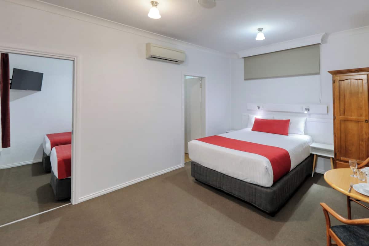 Una habitación de hotel con una cama, una mesa de comedor con sillas, un armario de madera y un televisor en la pared.