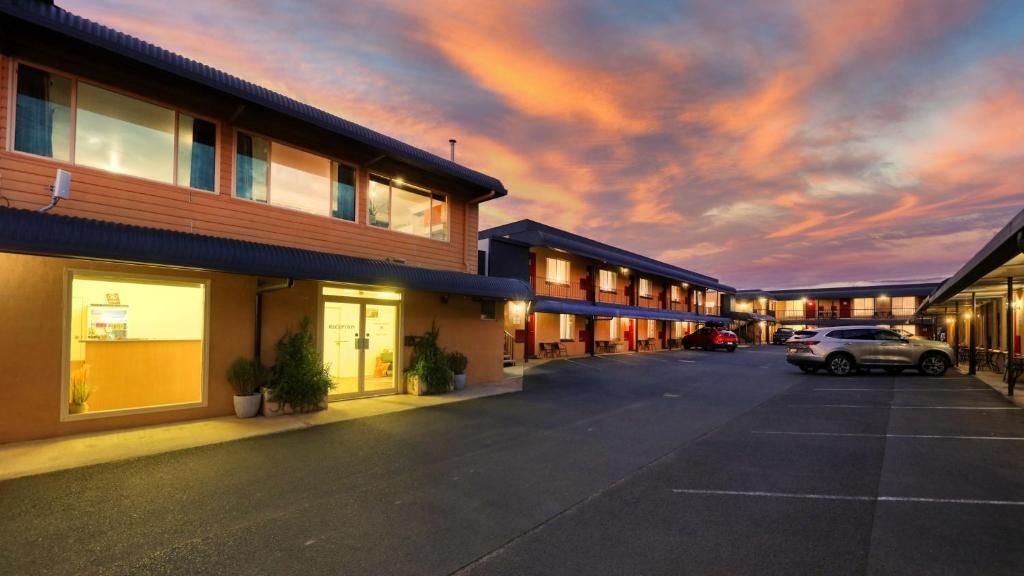 A motel with multiple rooms, a parking lot, and a sunset sky.