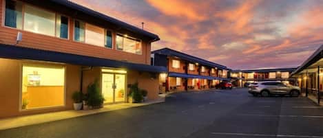 Un motel con varias habitaciones, un estacionamiento y un cielo al atardecer.
