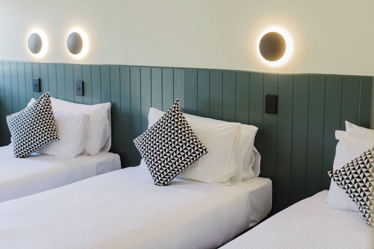 Twin beds with white linens and black and white patterned pillows, a green headboard, and wall-mounted circular lights.