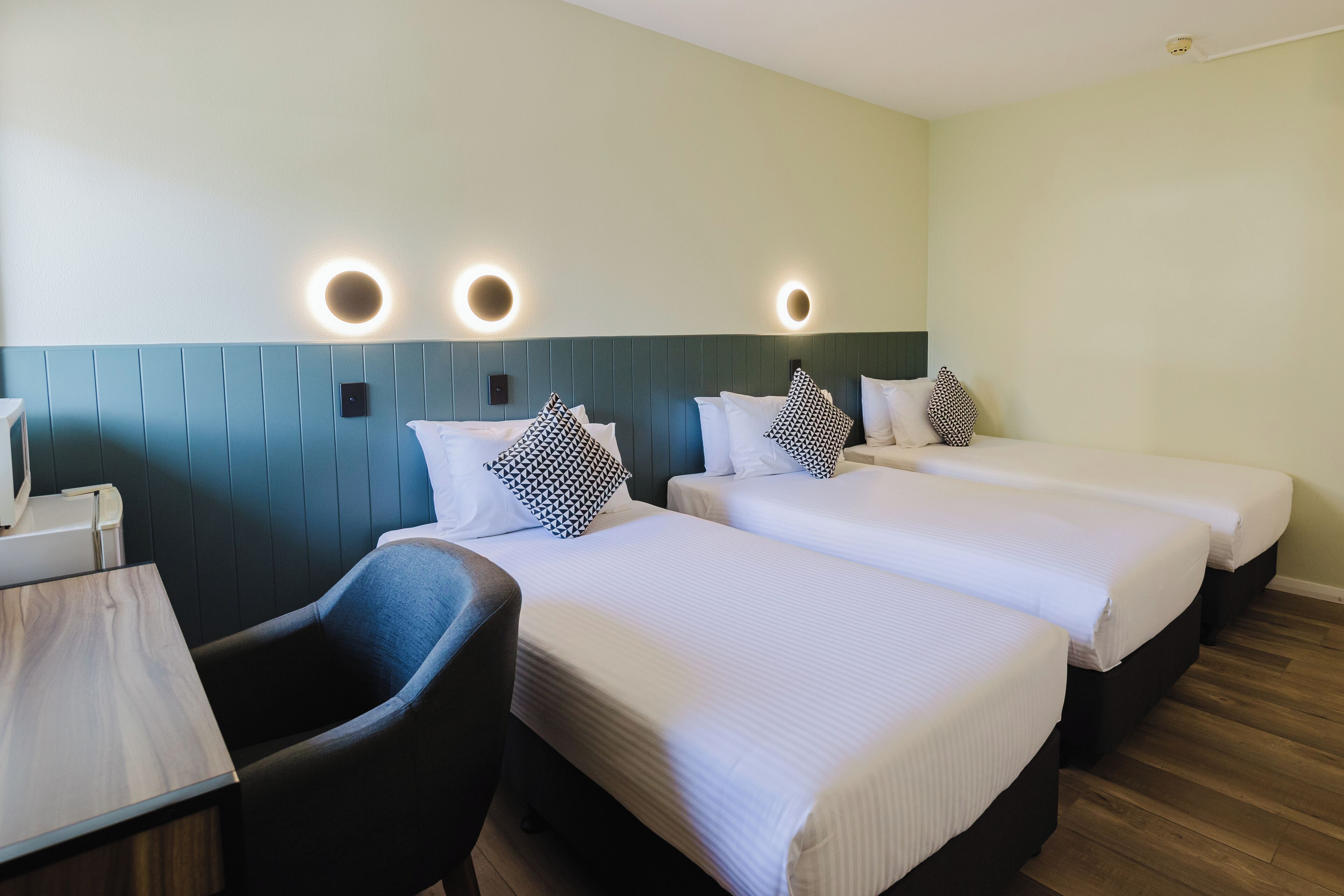Ett hotellrum med tre sängar, ett skrivbord och en stol.