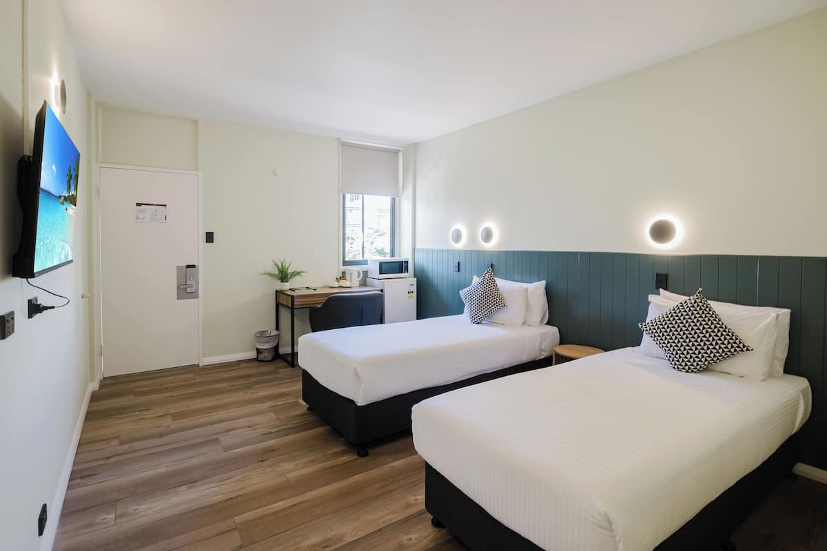 A hotel room with two beds, a desk, a chair, a TV, and a window.