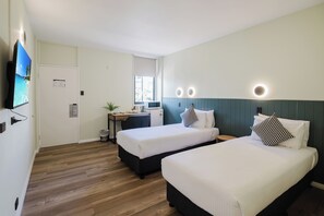 A hotel room with two beds, a desk, a chair, a TV, and a window.
