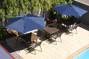 Un patio con una mesa, sillas y dos sombrillas, además de una piscina.