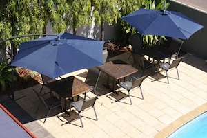 A patio with a table and chairs, two umbrellas, and a pool.