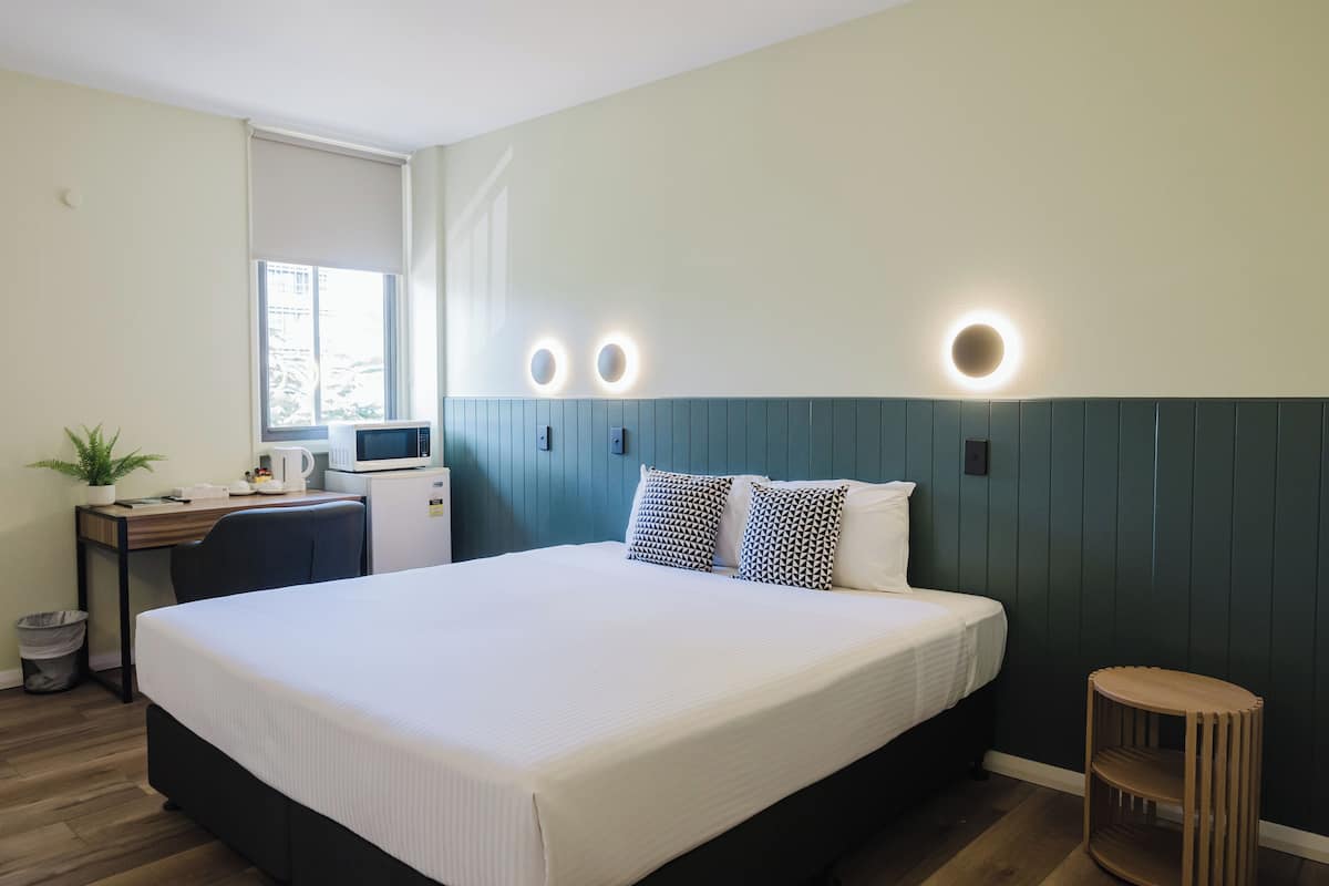 A neatly arranged hotel room with a large bed, a desk with a computer, a microwave, and a small plant.