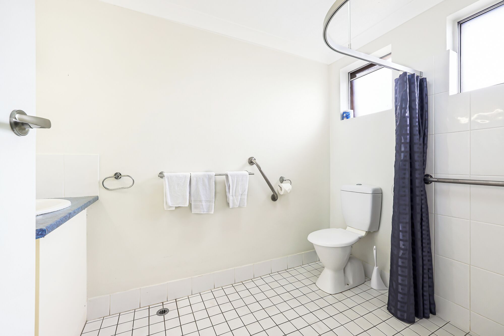 A bathroom with a white toilet, a shower curtain, a grab bar, and a towel rack.