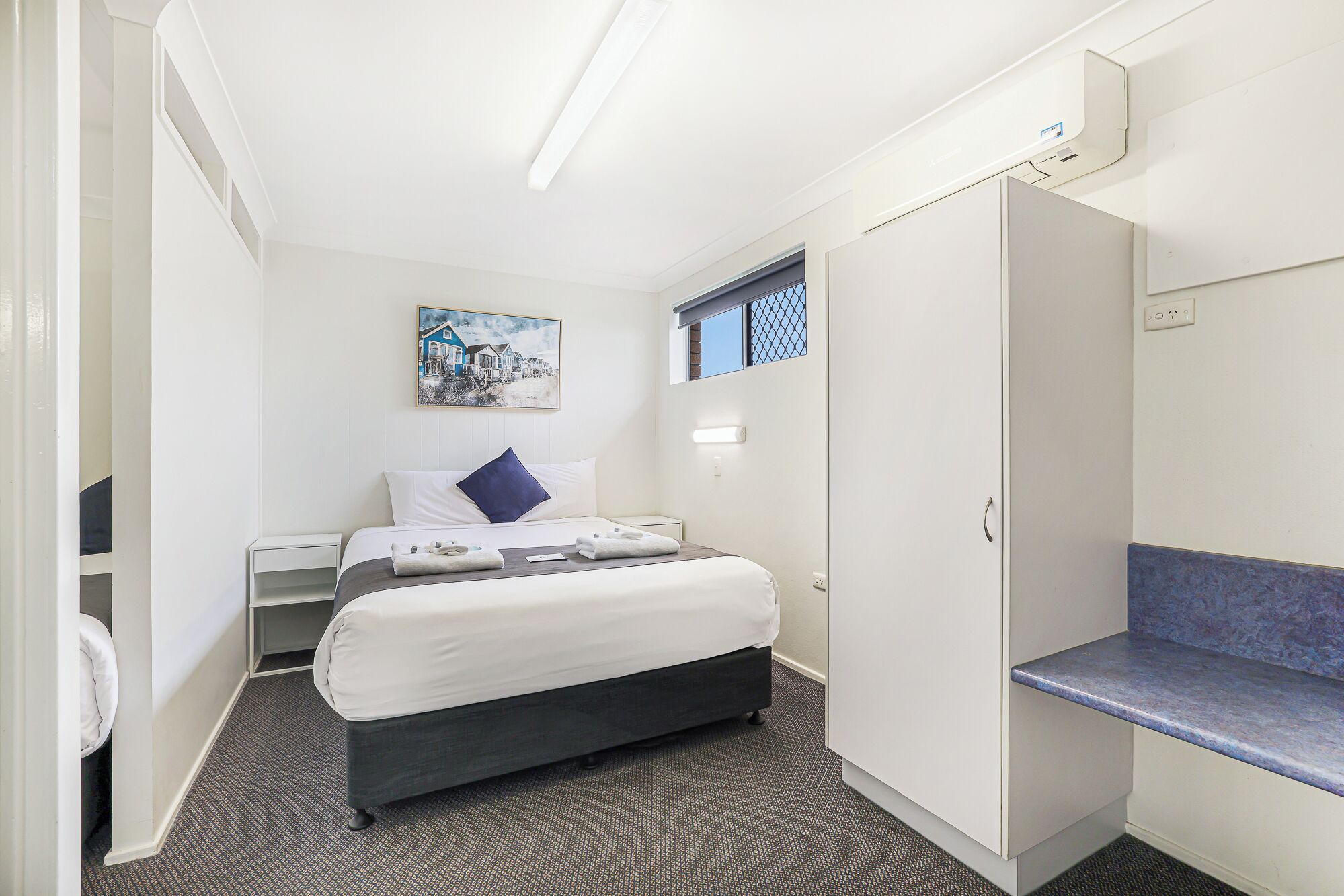 Une chambre d’hôtel avec un lit, un bureau, une armoire et une fenêtre donnant sur des maisons.