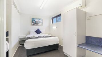 Une chambre d’hôtel avec un lit, un bureau, une armoire et une fenêtre donnant sur des maisons.