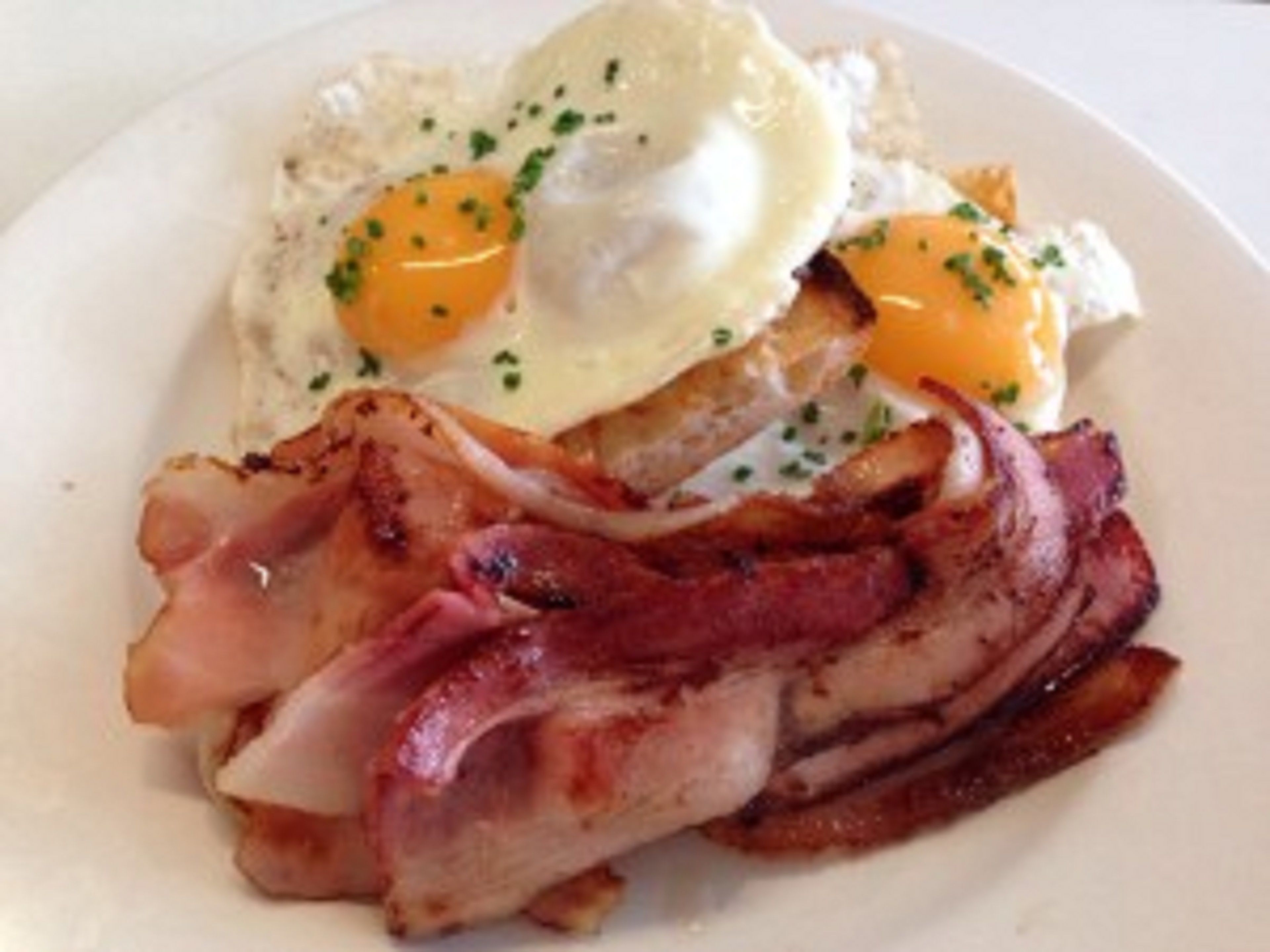 Une assiette avec deux œufs au plat, une tranche de pain grillé et une tranche de bacon.