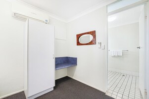 Un baño con inodoro blanco, lavamanos azul, espejo con marco de madera y zona de ducha con piso de baldosas.