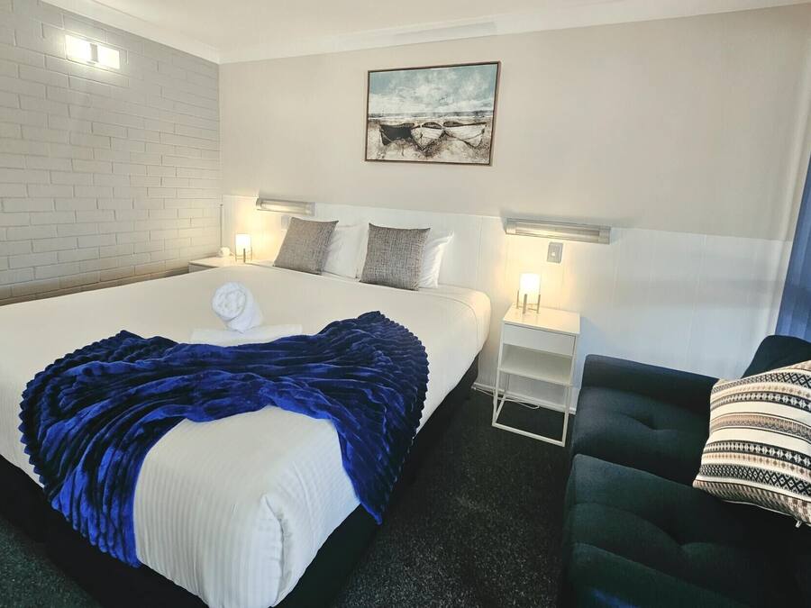 A hotel room with a large bed, a bedside table, a chair, a wall-mounted picture, and a window with curtains.
