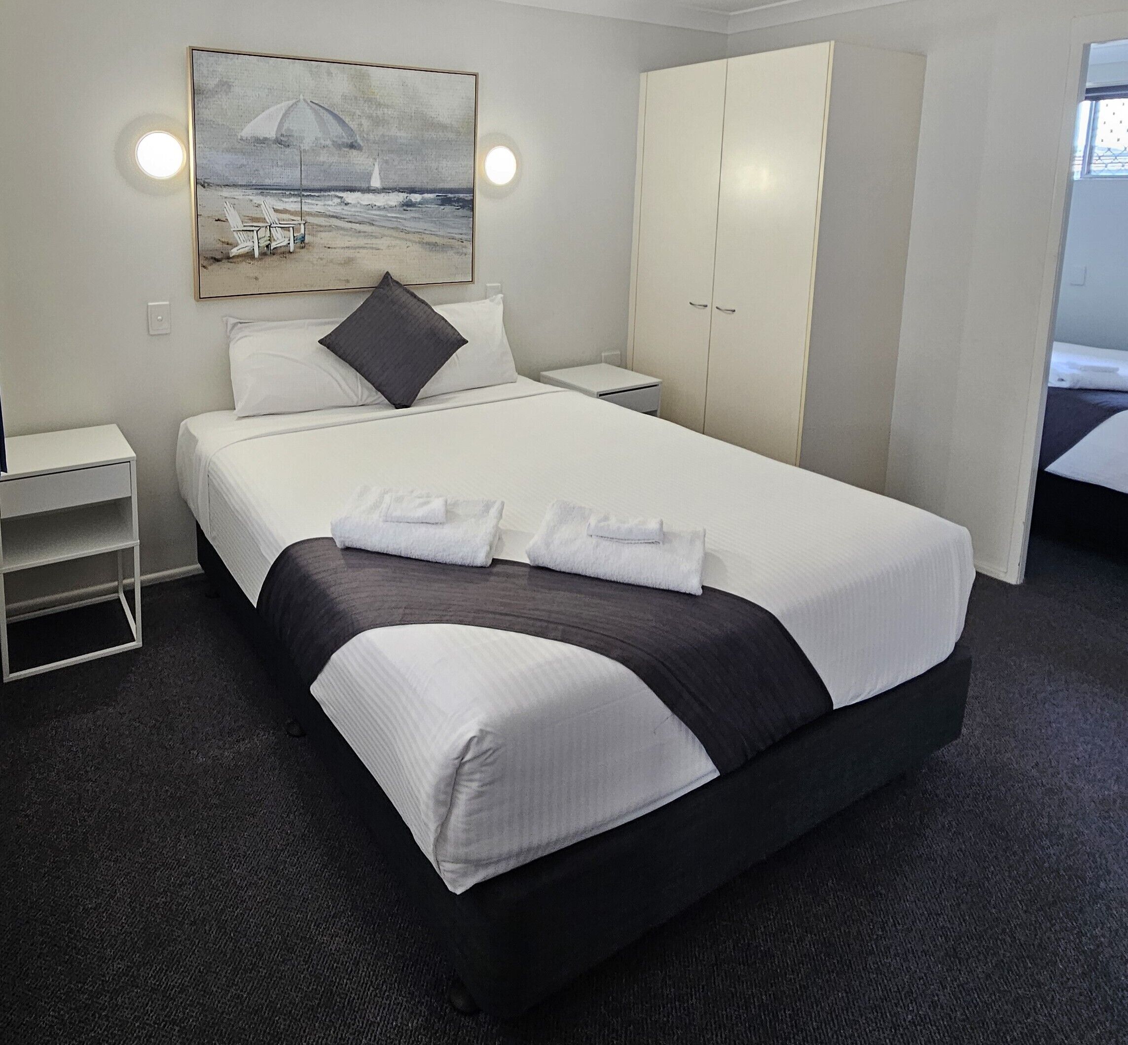 A hotel room with a bed, a nightstand, a wardrobe, and a painting on the wall.