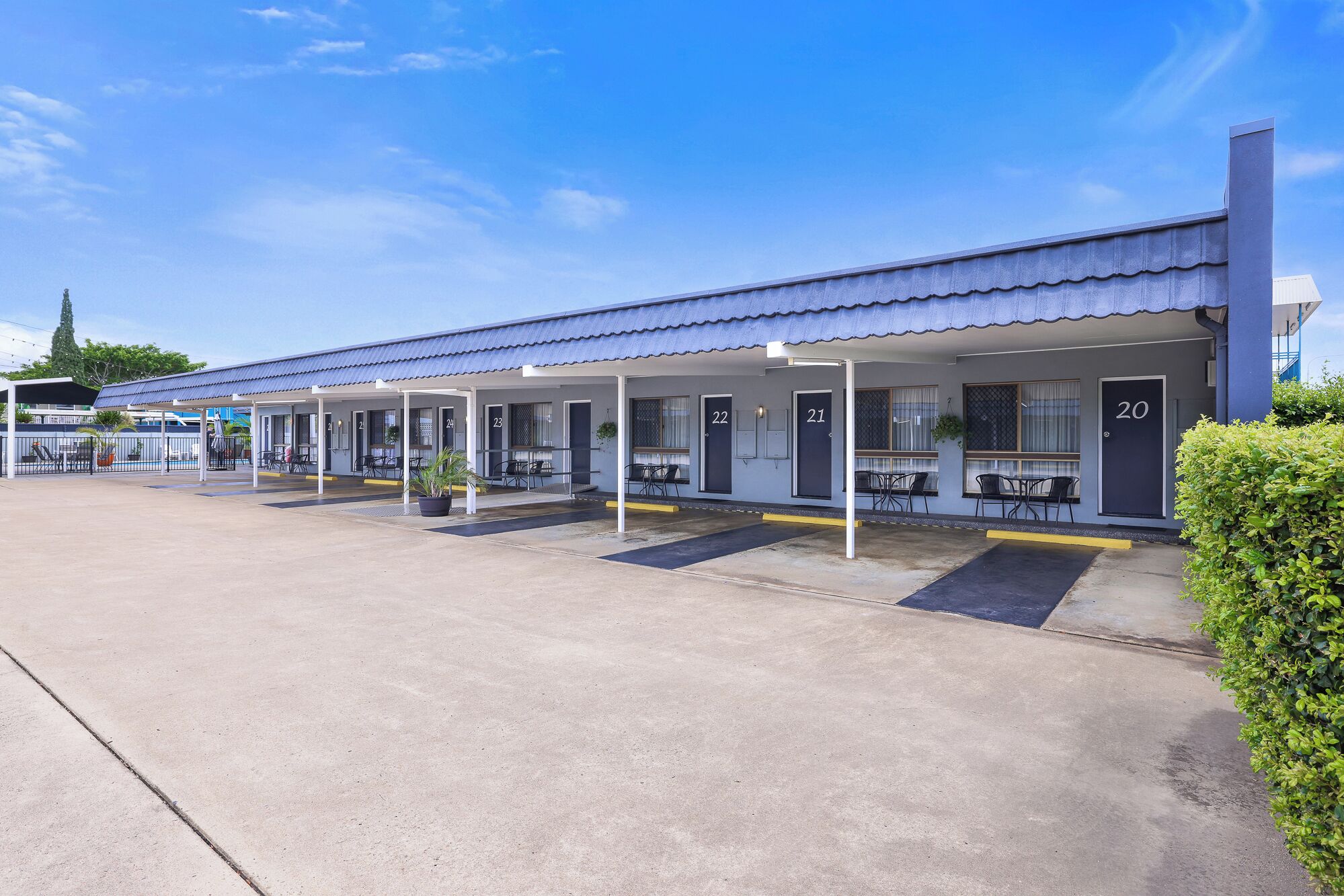 Un motel con habitaciones numeradas, asientos al aire libre y un estacionamiento techado.