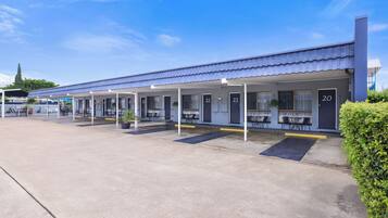 Un motel con habitaciones numeradas, asientos al aire libre y un estacionamiento techado.