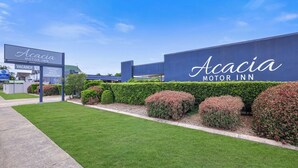 Acacia Motor Inn -hotellin ulkopuoli: suuri kyltti, jossa on hotellin nimi, hyvin hoidettu nurmikko ja siististi leikatut pensaat.